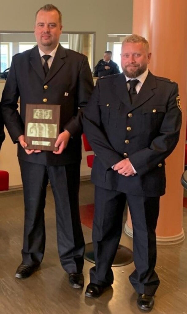 Joki pitää kädessään palkintolaattaa. Joki ja Koskinen ovat pukeutuneet palokuntalaisen juhlapukuun. 