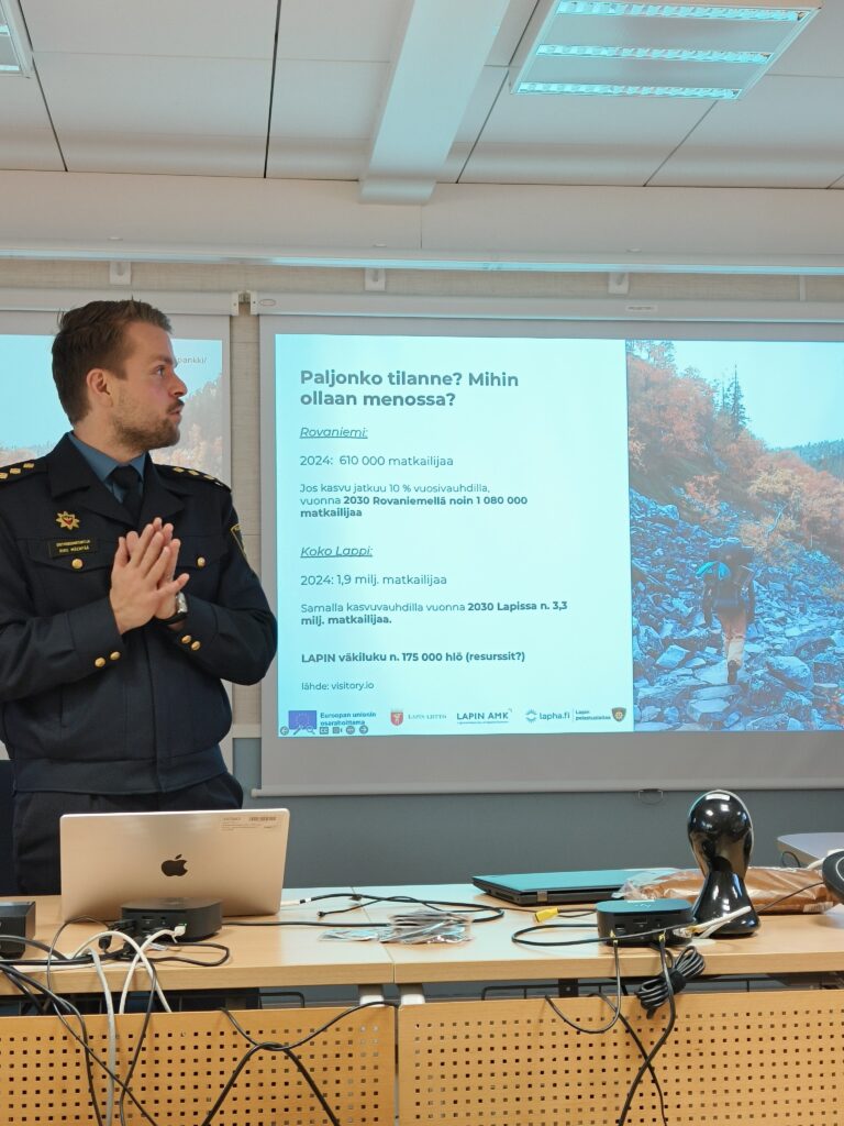 Kuvassa Mäenpää esittämässä diaa Lapin matkailun tilanteesta. Rovaniemellä kävi 2024 610 000 matkailijaa. Jos kasvu jatkuu 10 % vuosivauhtia, vuonna 2023 Rovaniemellä on noin 1 080 000 matkailijaa. 