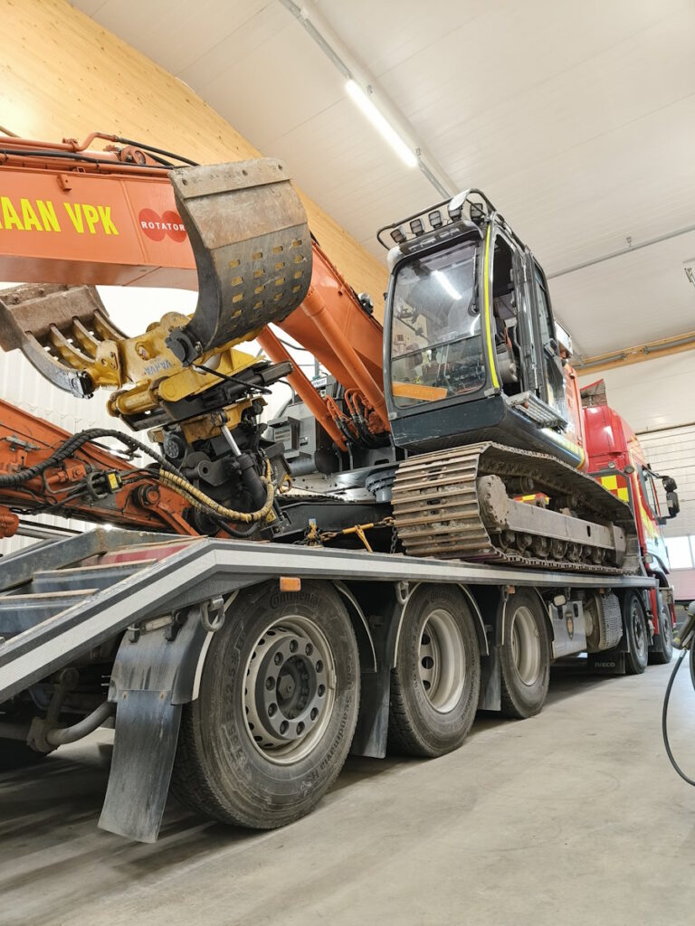 Telakaivukone kuljetusajoneuvon kyydissä kalustohallissa. 