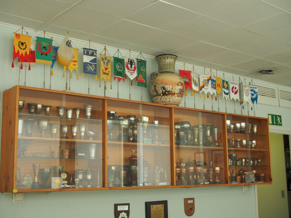 Seinälle kiinnitetty palkintokaappi, missä on lukuisia erilaisia pokaaleja ja palkintoja.
