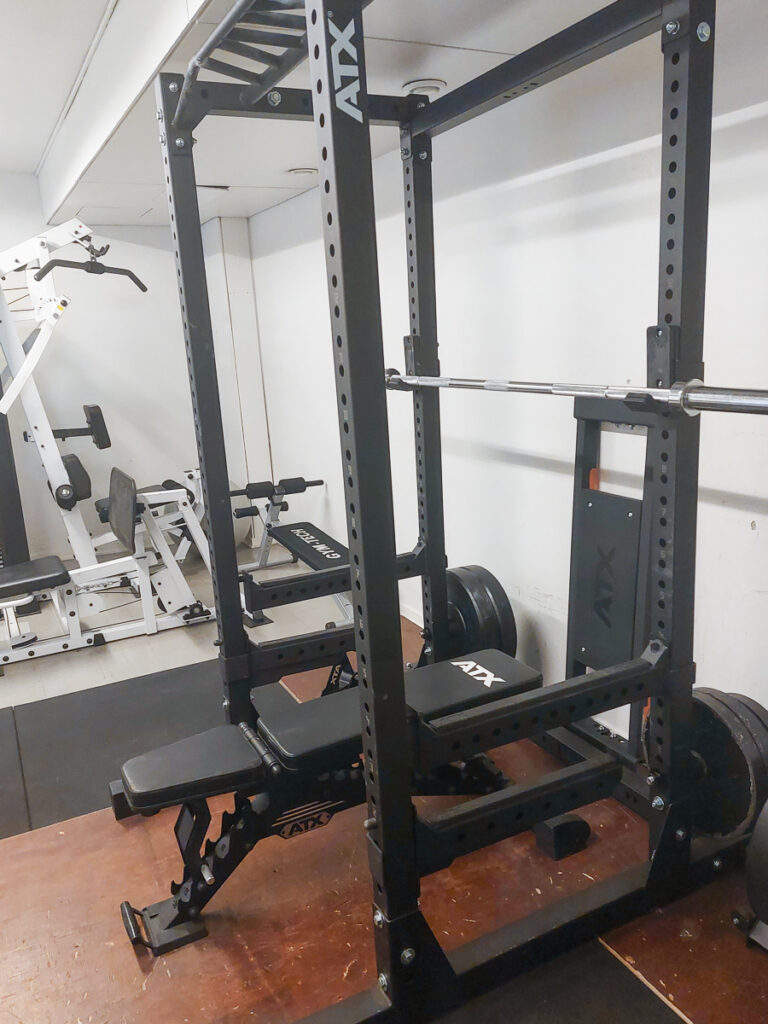 Kuva pienellä kuntosalilla olevista treenilaitteista. Etualalla painonnostopenkki. 