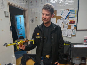 Riskilä on toimistossa virkapuku päällä ja pitää kädessään dronea.