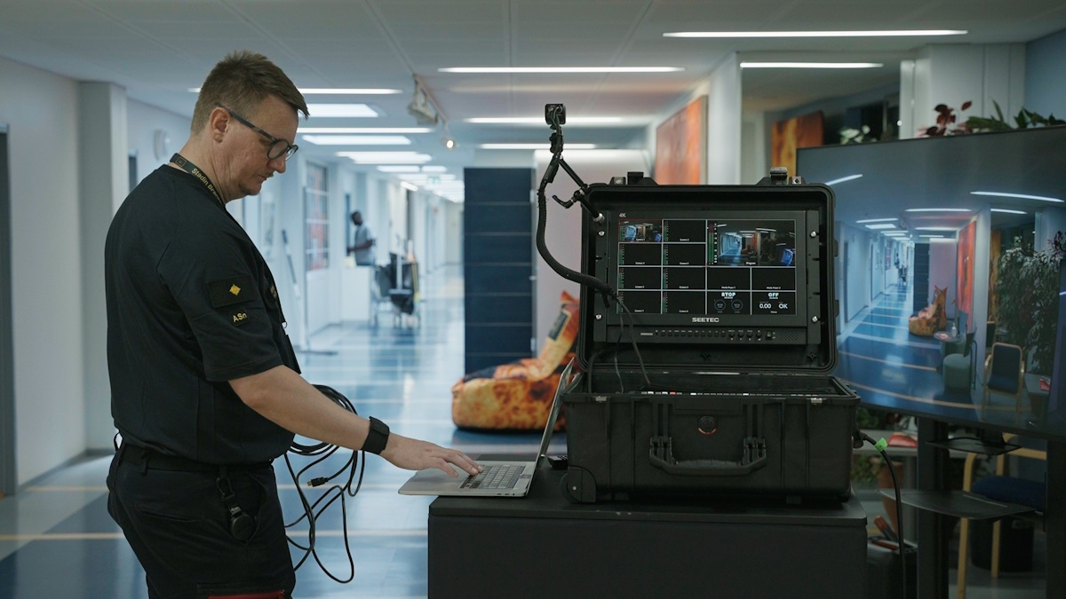 Kuvassa musta livesalkku on pöydällä ja siihen on kytketty kannettava tietokone, jota pelastuslaitoksen henkilöstöön kuuluva ihminen käyttää. Kuva on otettu pelastuslaitoksen käytävältä.